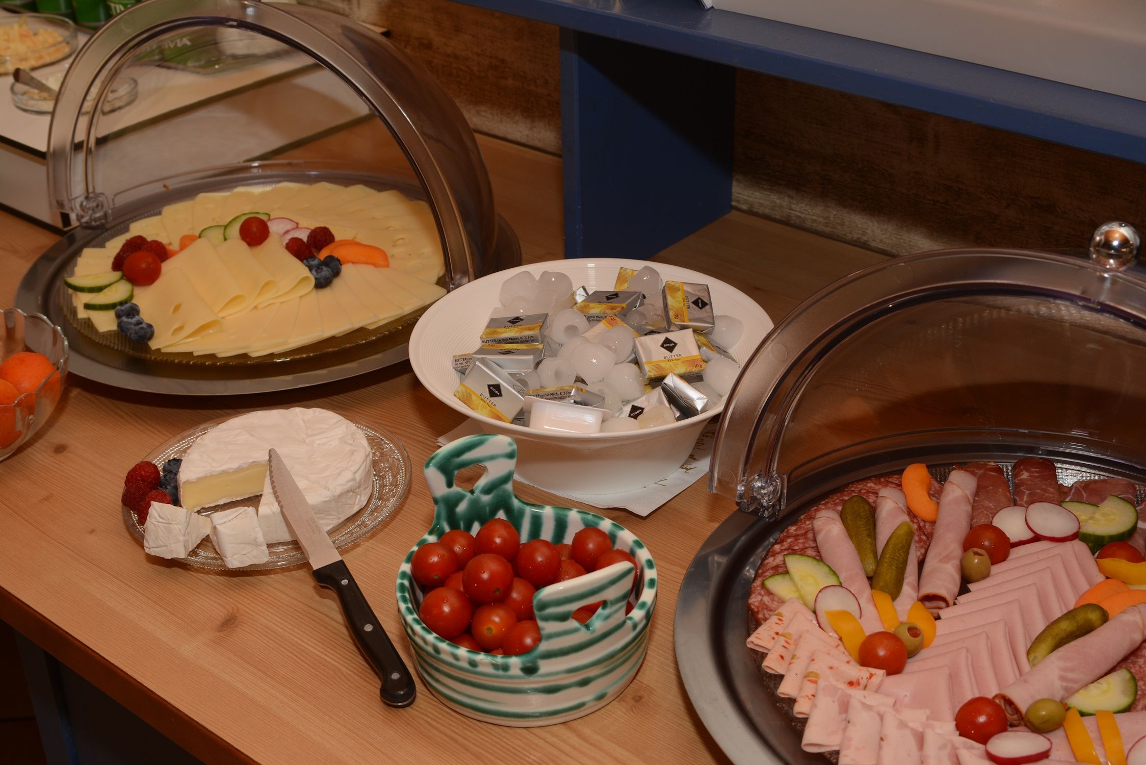 Frühstücksbuffet mit Käse, Wurst, Tomaten, Butter und Camembert.