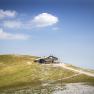 Eine Berghütte auf einem Hügel mit blauem Himmel und Wolken im Hintergrund.