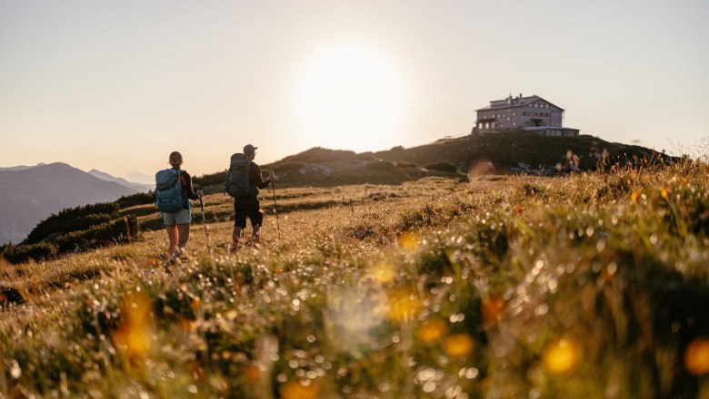 Die sanften H&uuml;gel der Wiener Alpen laden zu einem unvergesslichen Abenteuer ein. Zwei Wanderer genie&szlig;en die goldene Abendsonne, w&auml;hrend sie durch die bl&uuml;henden Wiesen streifen. Die atemberaubende Aussicht und die frische Bergluft schaffen eine perfekte Kulisse f&uuml;r unvergessliche Erinnerungen.