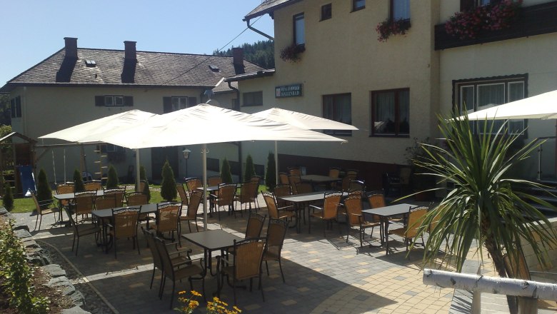 Außenbereich einer Pension mit Tischen, Stühlen und Sonnenschirmen.
