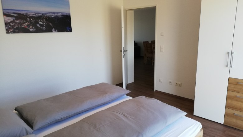 Modernes Schlafzimmer mit Doppelbett, weißem Kleiderschrank und Landschaftsbild an der Wand.