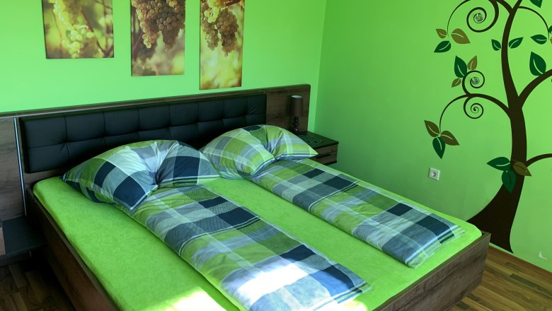 Schlafzimmer mit gr&uuml;nem Thema, Doppelbett, Wandbilder von Trauben und Baumdekoration.