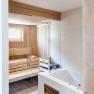 Innenansicht einer modernen Sauna mit Holzverkleidung und Glaswand, daneben eine weiße Badewanne.