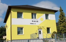 Gelbes Haus mit der Aufschrift 'Haus' und einer Sonne auf der Fassade.