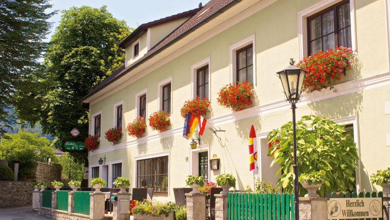 Ein traditionelles Gasthaus mit grüner Fassade und roten Blumen in Blumenkästen vor den Fenstern.