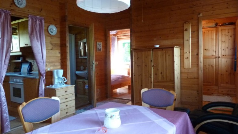 Innenansicht eines gemütlichen Ferienhauses mit Holzwänden, Esstisch und Küchenbereich.