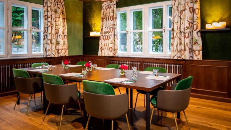 Ein Jagdzimmer mit Holztisch, grünen Stühlen und Geweihleuchter.