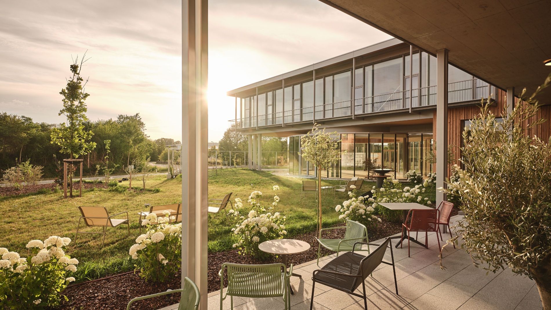 Moderne Terrasse mit Gartenmöbeln und Blumen vor einem Gebäude bei Sonnenuntergang.