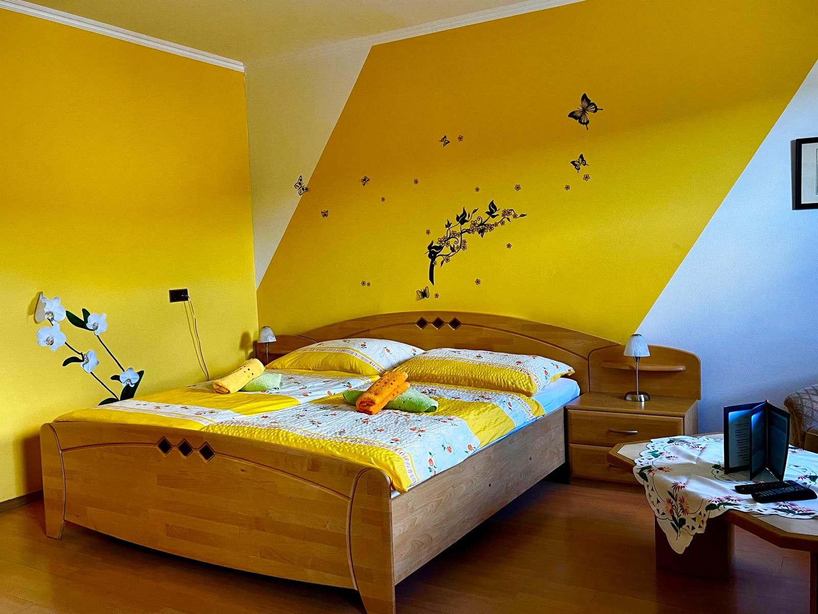 Gemütliches Schlafzimmer mit gelber Wand, Doppelbett und dekorativen Schmetterlingen an der Wand.