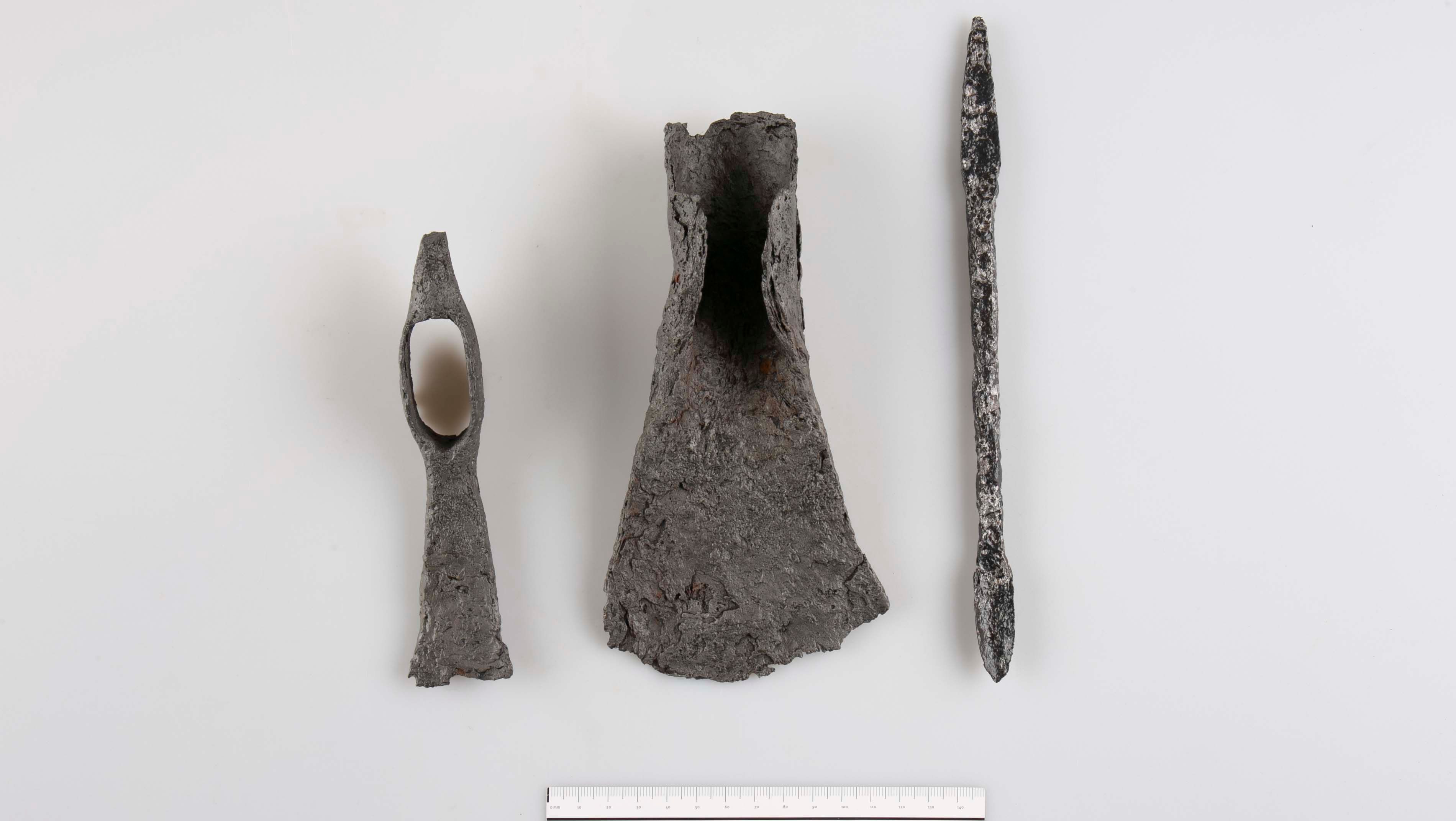 Drei archäologische Metallobjekte auf weißem Hintergrund mit Maßstab unten.