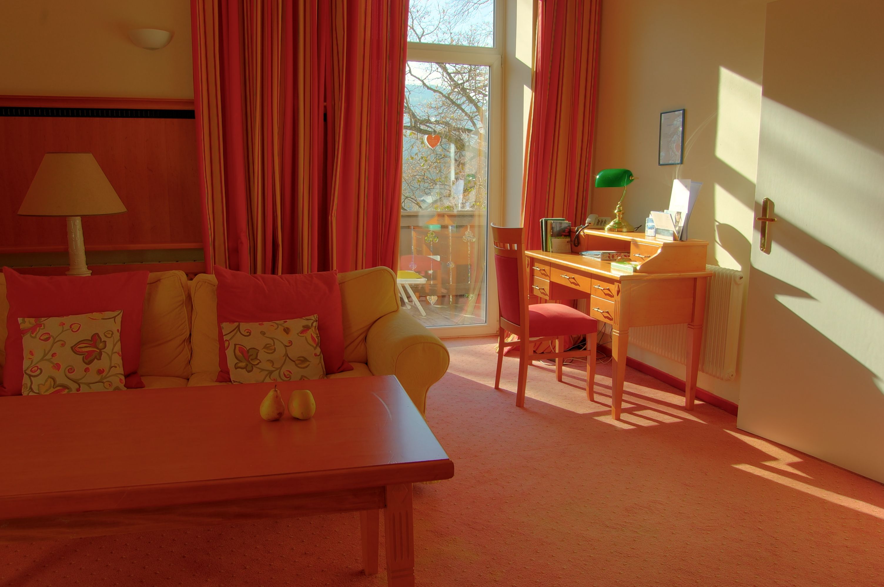 Ein gemütliches Zimmer mit Sofa, Schreibtisch und großem Fenster mit Vorhängen.