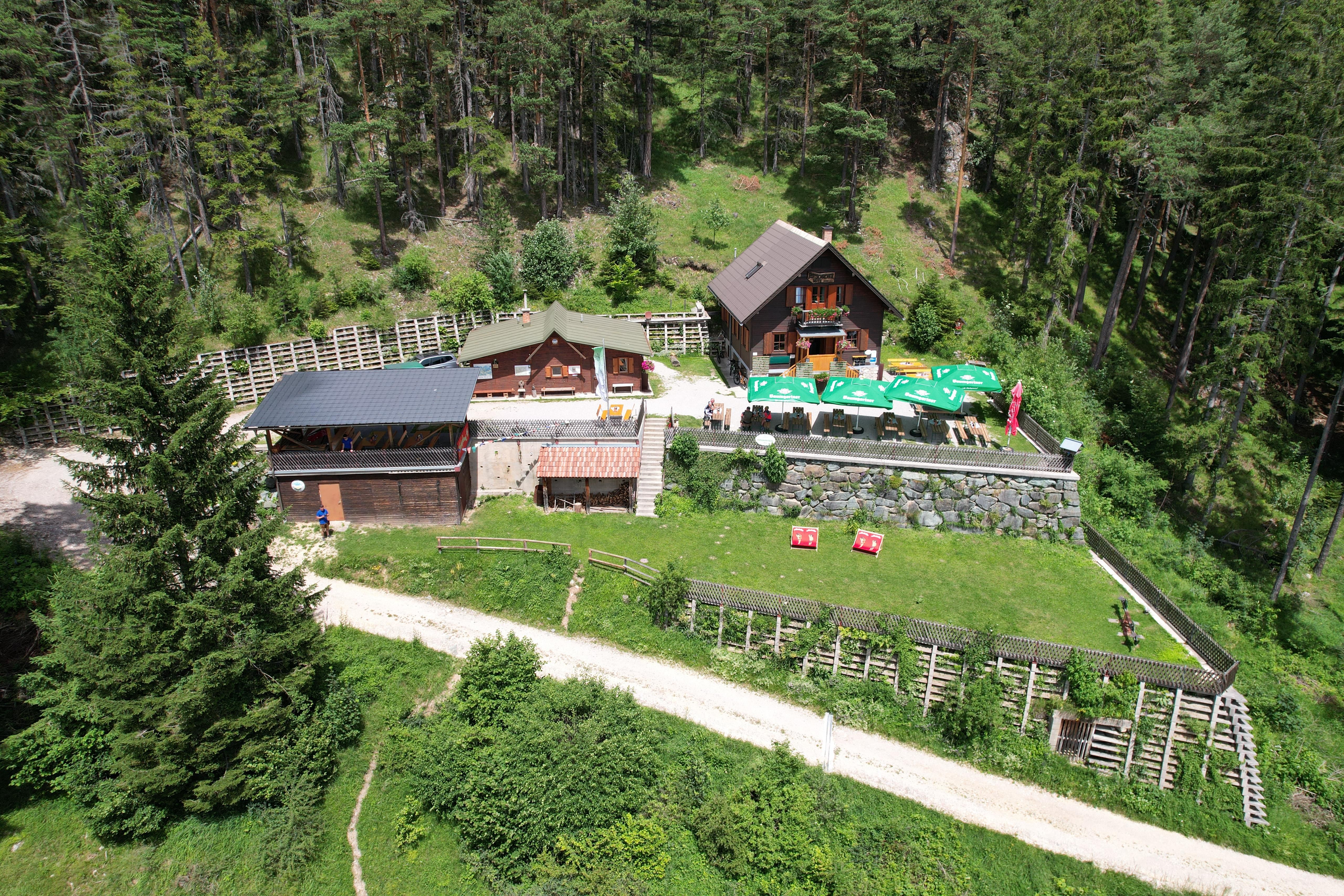 Luftaufnahme der Potschacherhütte in einem Waldgebiet mit umliegenden Bäumen und einer Terrasse mit Sonnenschirmen.