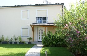 Au&szlig;enansicht eines zweist&ouml;ckigen Hauses mit Garten und Pflanzen.