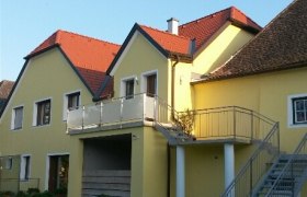 Gelbes Gebäude mit roten Dächern und Außentreppe.