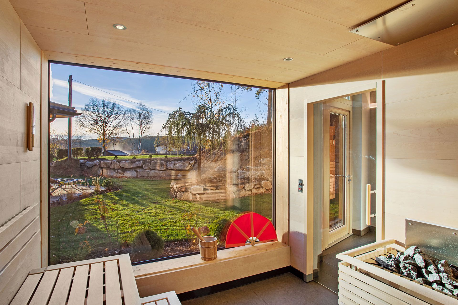 Innenansicht einer modernen Sauna mit großem Fenster und Blick auf einen Garten.