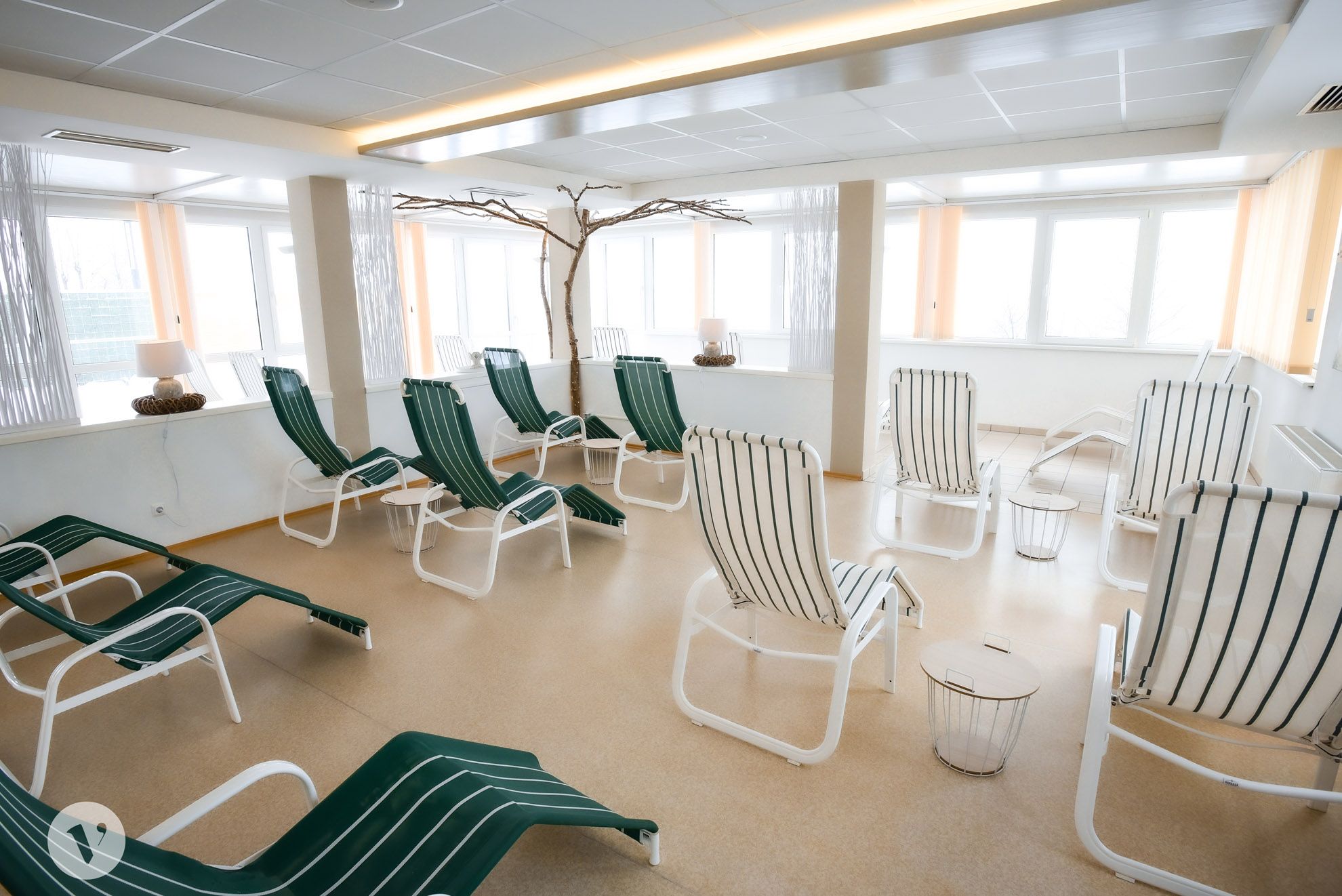 Ein heller Ruhebereich mit mehreren grünen Liegestühlen und kleinen Tischen.