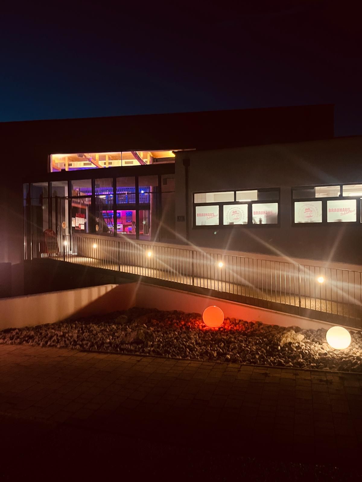 Nachtaufnahme Brauhaus Schwechat mit beleuchteten Fenstern und farbigen Kugelleuchten im Vordergrund.