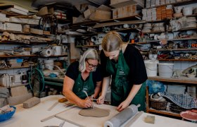 Zwei Frauen arbeiten in einer Keramikwerkstatt an einem Tonst&uuml;ck.