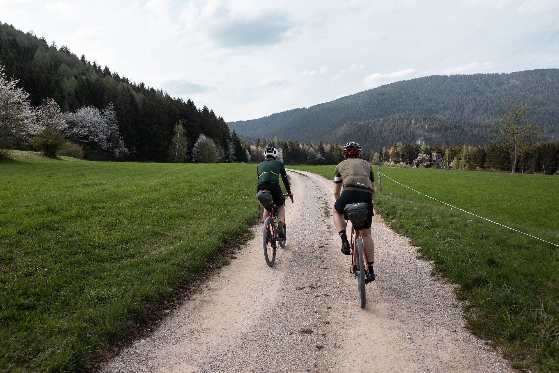 Zwei Radfahrer gleiten entspannt auf einem schmalen Schotterweg durch die malerische Landschaft der Wiener Alpen. Umgeben von saftigem Grün und majestätischen Bergen, erleben sie die Freiheit und die Schönheit der Natur in vollen Zügen. Der Duft von frischem Gras und die sanfte Brise machen diese Radtour zu einem unvergesslichen Erlebnis.