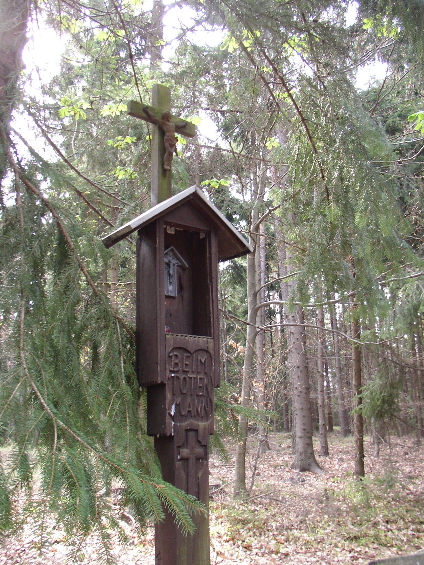 Holzkreuz mit Christusfigur im Wald, beschriftet mit 'Beim Toten Mann'.