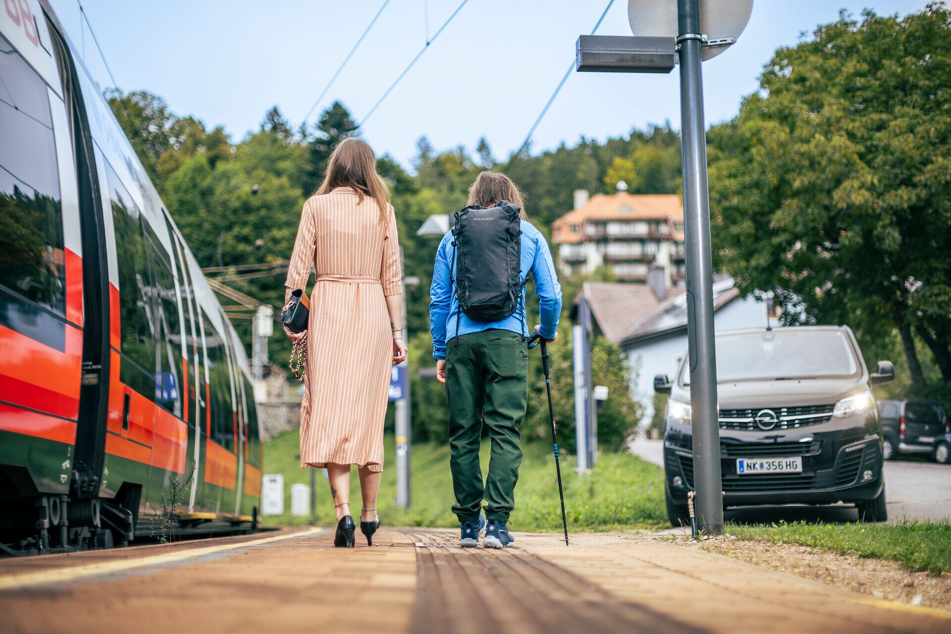 Ein schwarzer Kleinbus, der RUF Bus, holt gerade eine Frau in einem schönen orangen Kleid und einen Wanderer ab. 