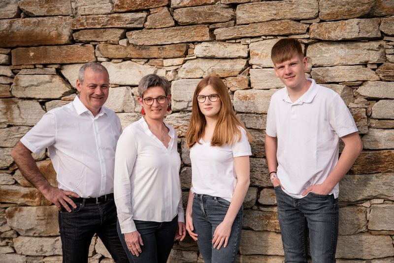 Vier Personen stehen vor einer Steinmauer, alle in weiß gekleidet.