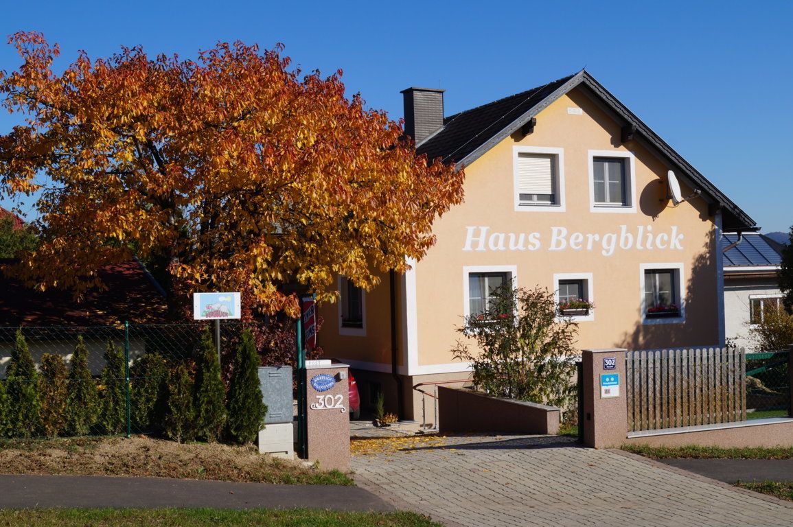 Ein gelbes Haus mit der Aufschrift 'Haus Bergblick' und einem herbstlichen Baum davor.