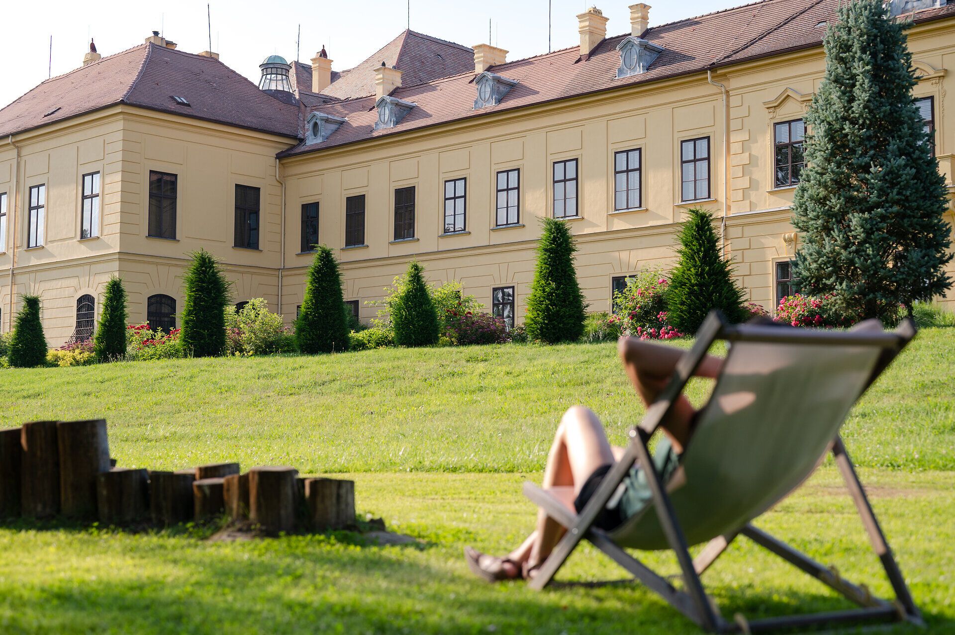 Frau in einem Liegestuhl auf einer grünen Wiese blickt auf Schloss Eckartsau. 