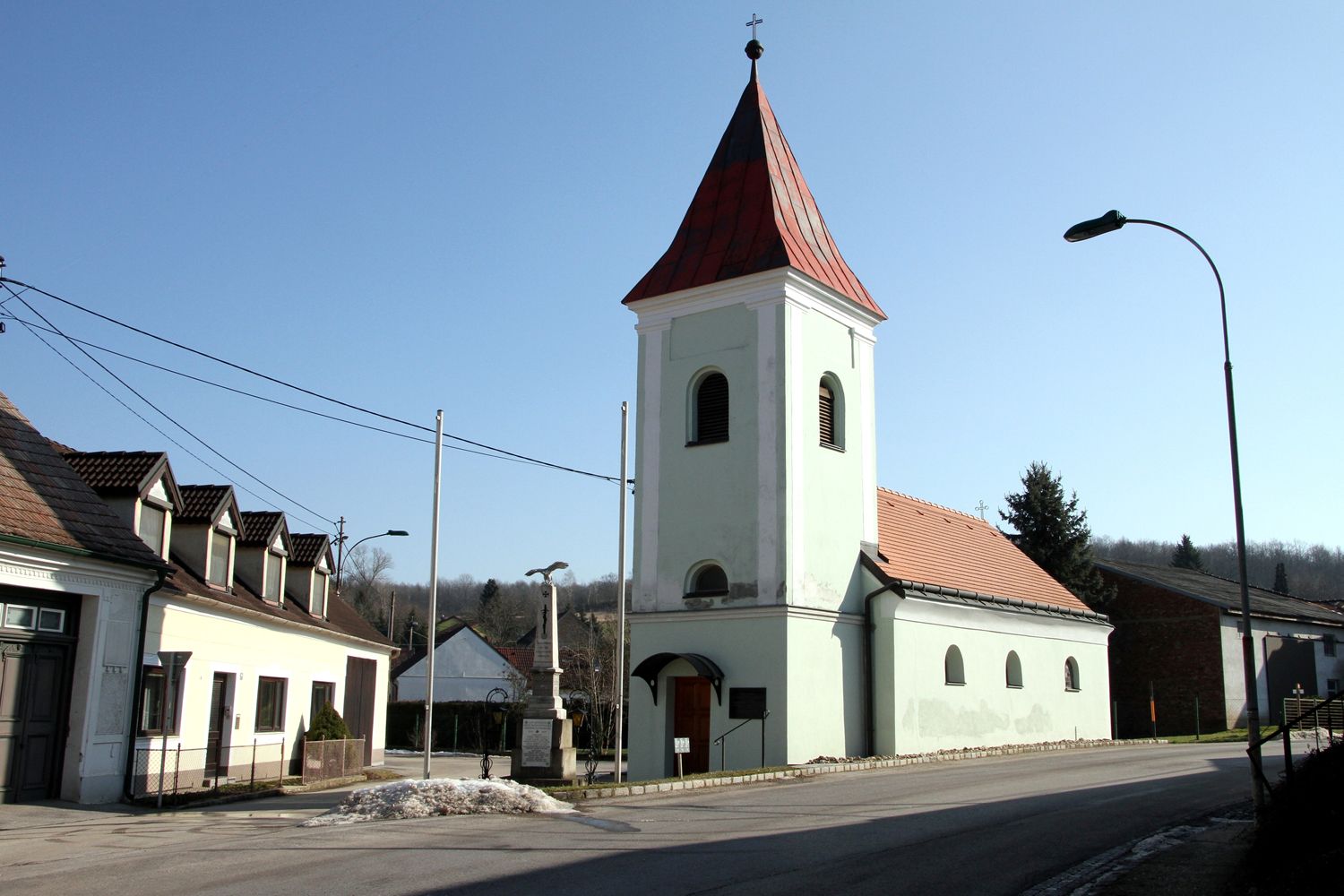 Kirche mit rotem Dach und Turm in einem Dorf bei klarem Himmel.