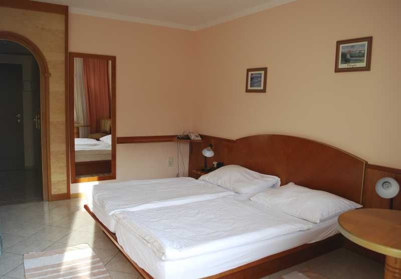 Hotelzimmer mit Doppelbett, Nachttischlampen und Wandbildern.