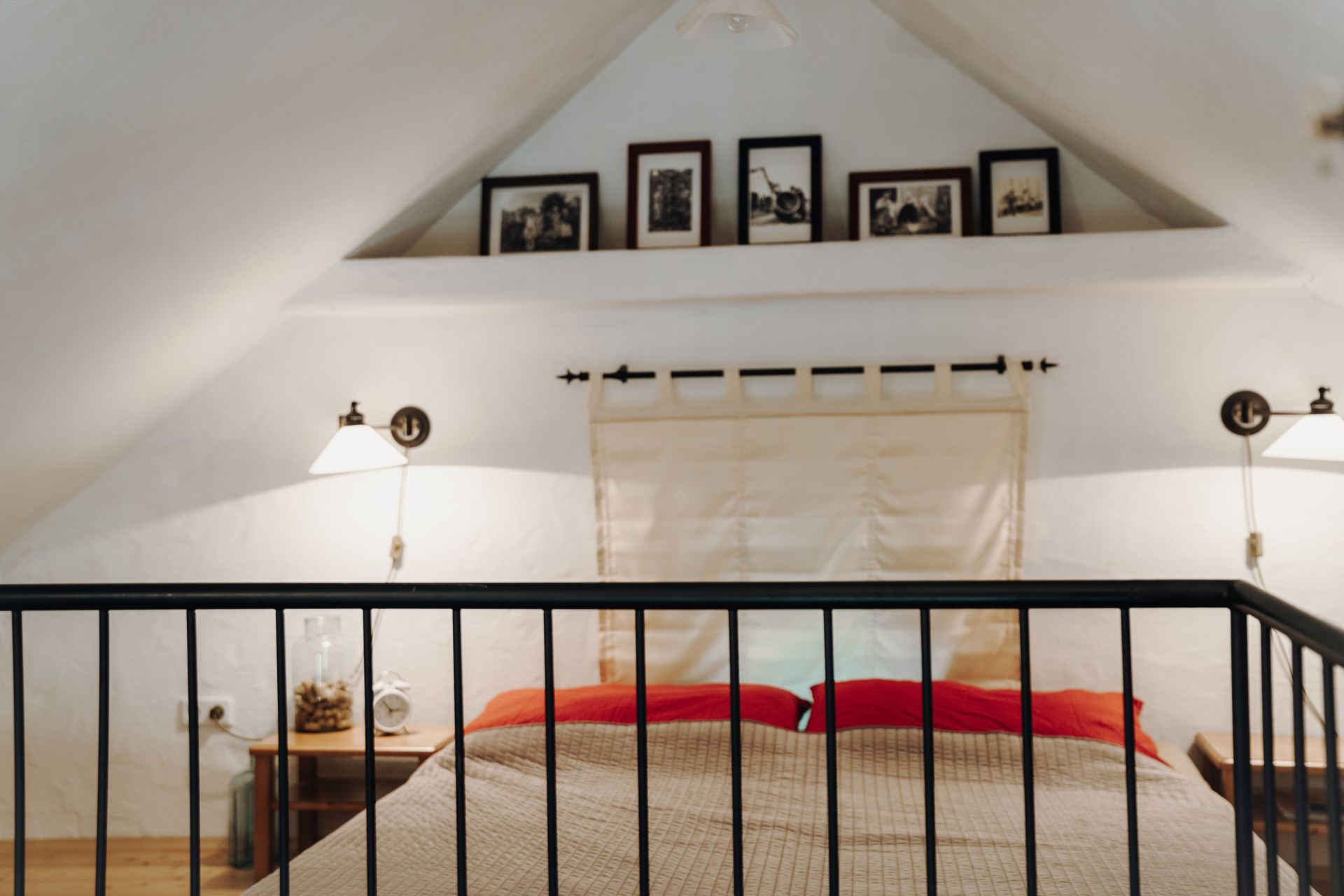 Dachzimmer mit Doppelbett, roten Kissen und Wandlampen.