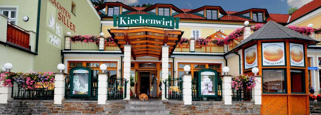 Eingang des Restaurants Kirchenwirt mit Blumen und Schildern.