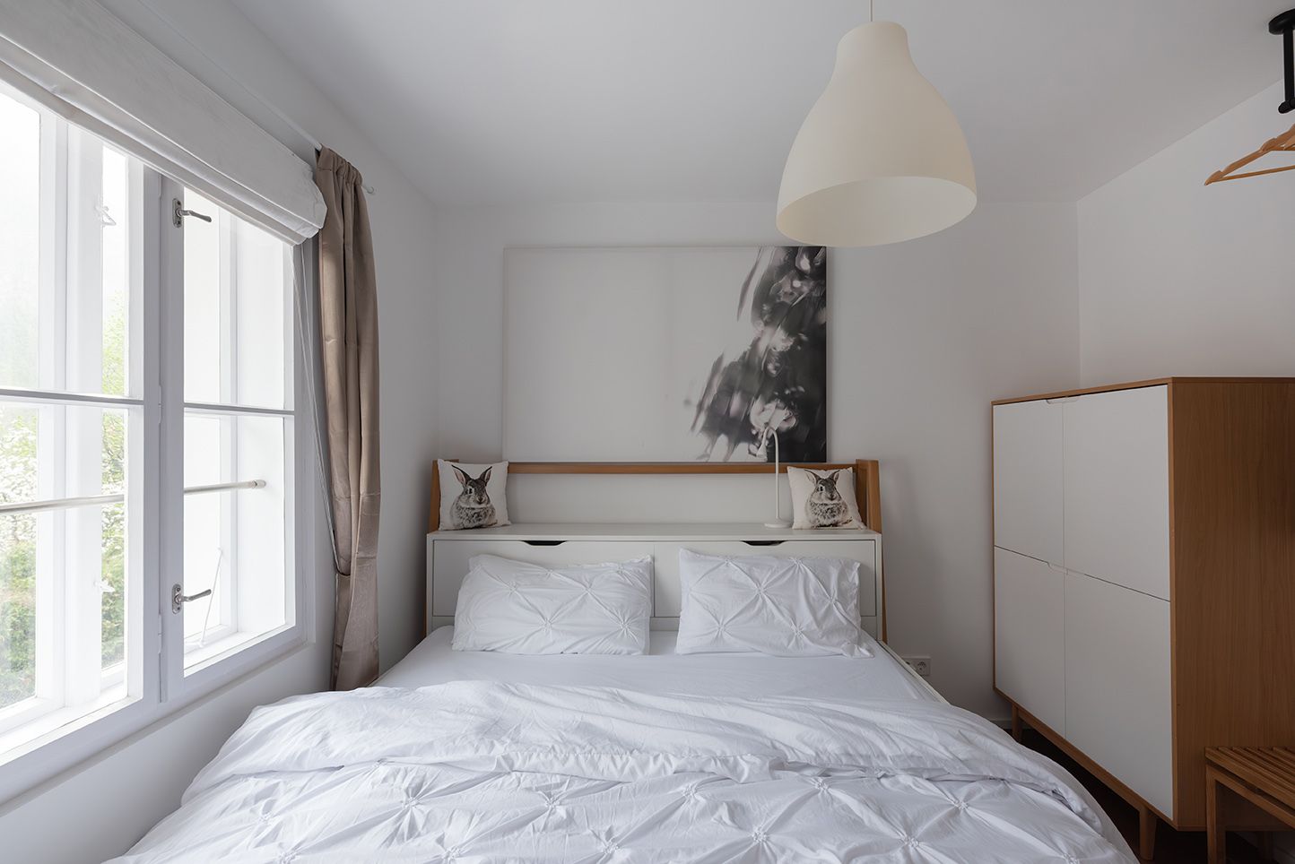 Modernes Schlafzimmer mit weißem Bett, Kissen mit Hasenmotiv und minimalistischer Dekoration.