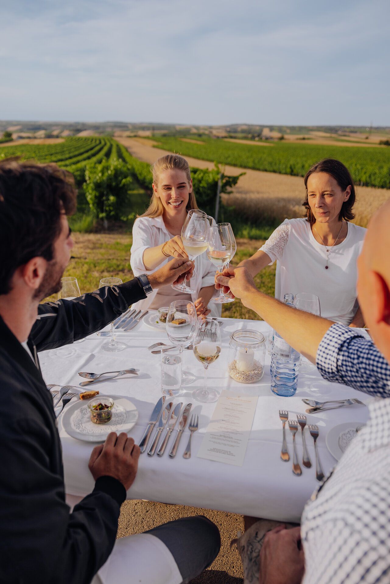 Inmitten der sanften Hügel des Weinviertels genießen Freunde ein festliches Mahl unter freiem Himmel. Die Tische sind liebevoll gedeckt, während die goldenen Strahlen der Abendsonne die Weinreben in ein warmes Licht tauchen. Ein unvergesslicher Moment der Geselligkeit und Kulinarik erwartet die Besucher.