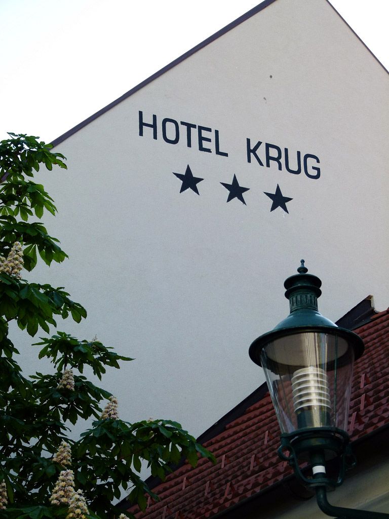 Fassade des Hotel Krug mit drei Sternen, Baum und Straßenlaterne.