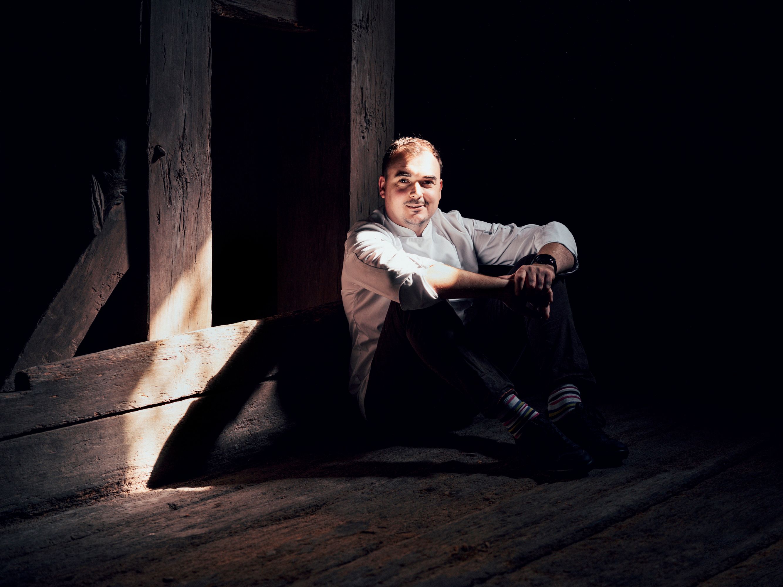 Mann in weißem Hemd sitzt im Schatten auf Holzboden.