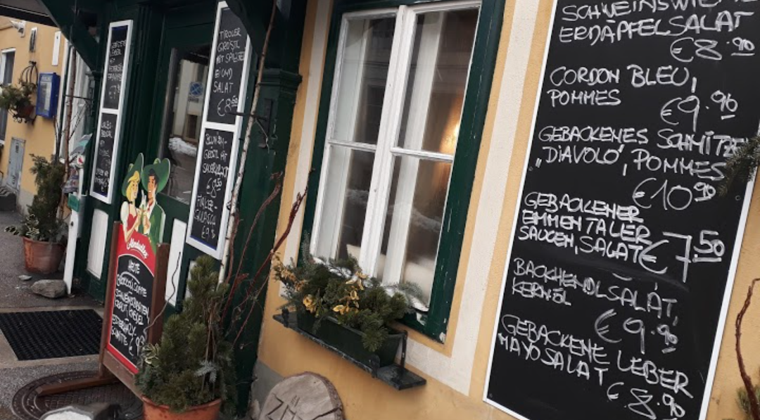 Eingang eines Wirtshauses mit mehreren Tafeln, die Speisen und Preise anzeigen.