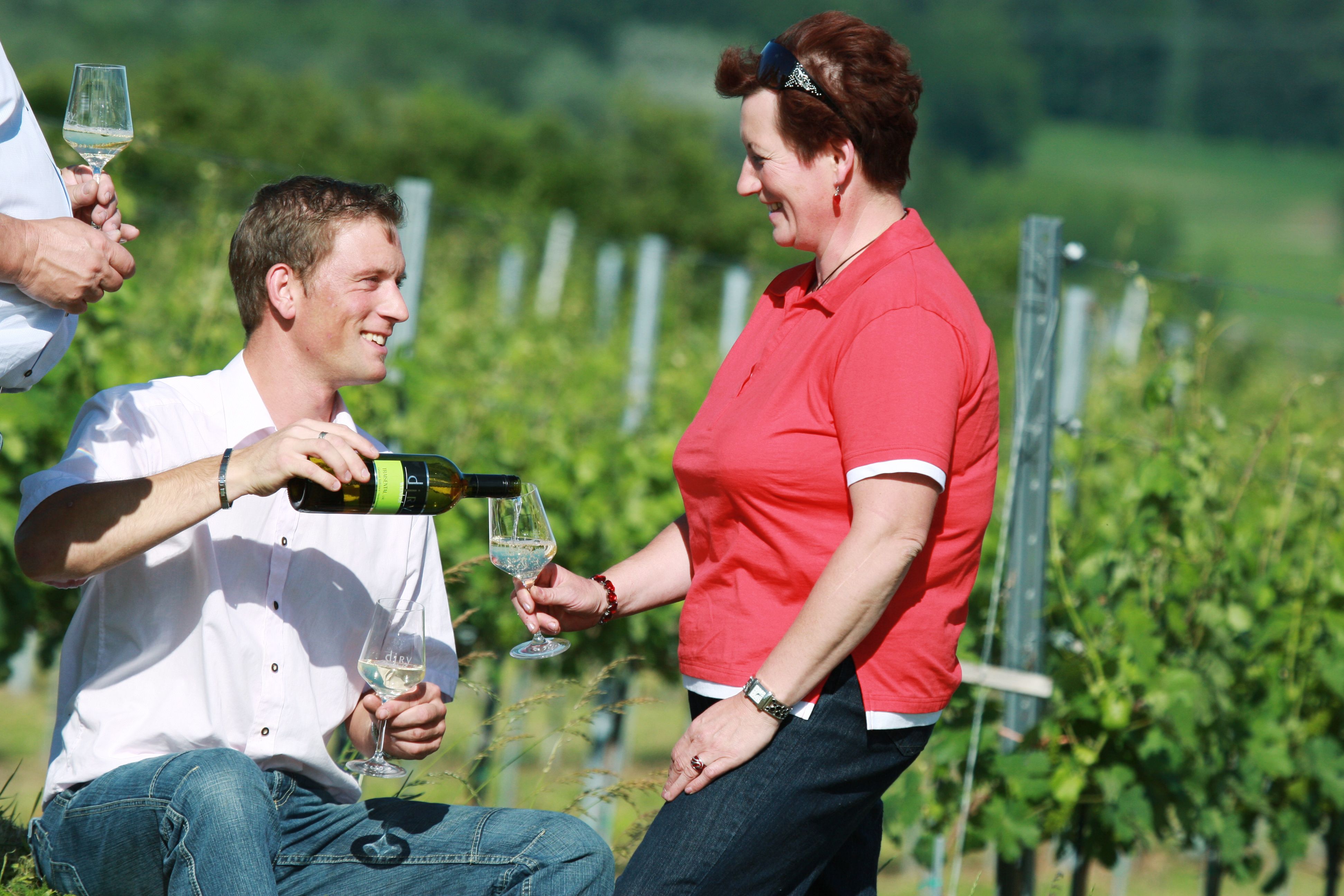 Ein Mann schenkt einer Frau Wein in einem Weinberg ein.