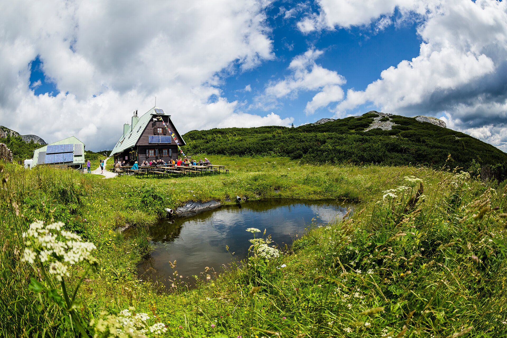 Umgeben von üppigen Wiesen und majestätischen Bergen, lädt die idyllische Hütte zu einer wohlverdienten Rast ein. Die klare Luft und das sanfte Plätschern des Wassers schaffen eine harmonische Atmosphäre, die Wanderer in ihren Bann zieht.