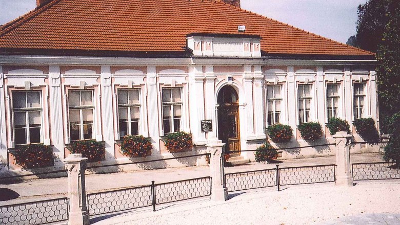 Historisches Gebäude mit rotem Ziegeldach und weißen Fensterrahmen, umgeben von Blumen.