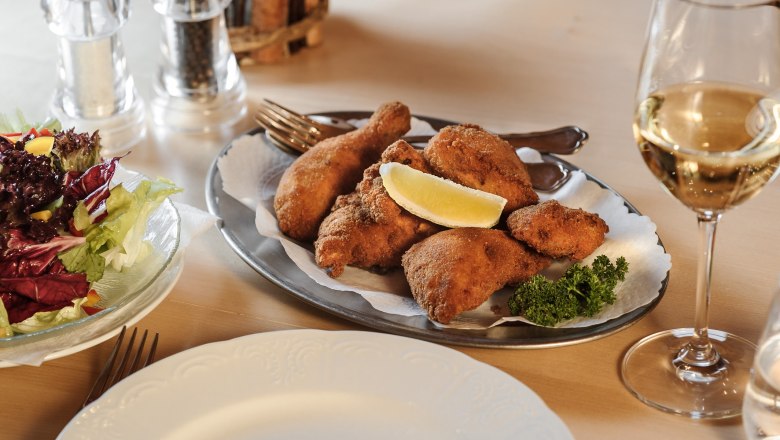 Ein Teller mit paniertem Hähnchen, Salat und einem Glas Weißwein auf einem Tisch.