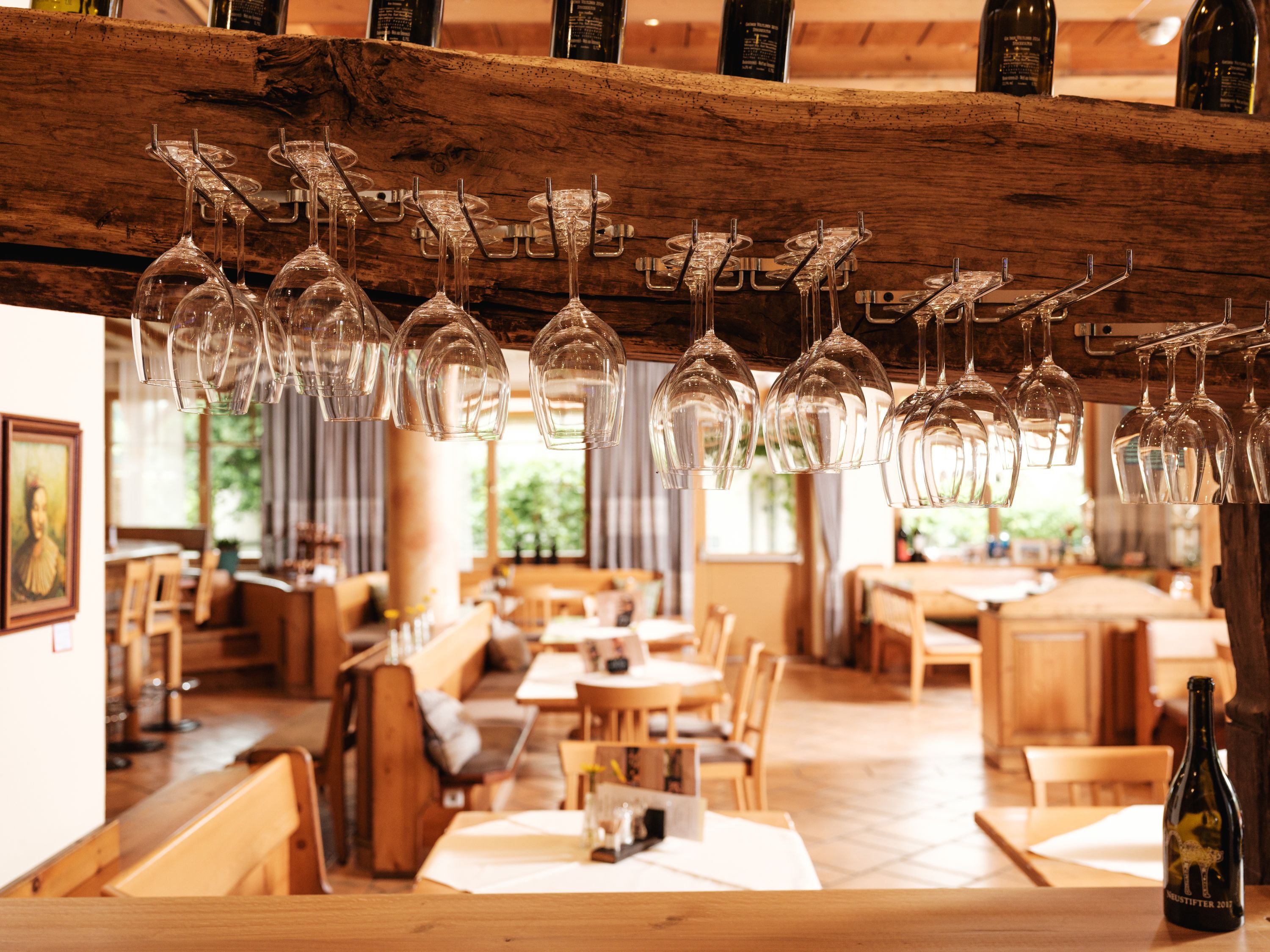 Innenansicht eines Restaurants mit hängenden Weingläsern und Holzmöbeln.