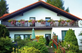 Ein zweist&ouml;ckiges Haus mit Balkon und Blumen.