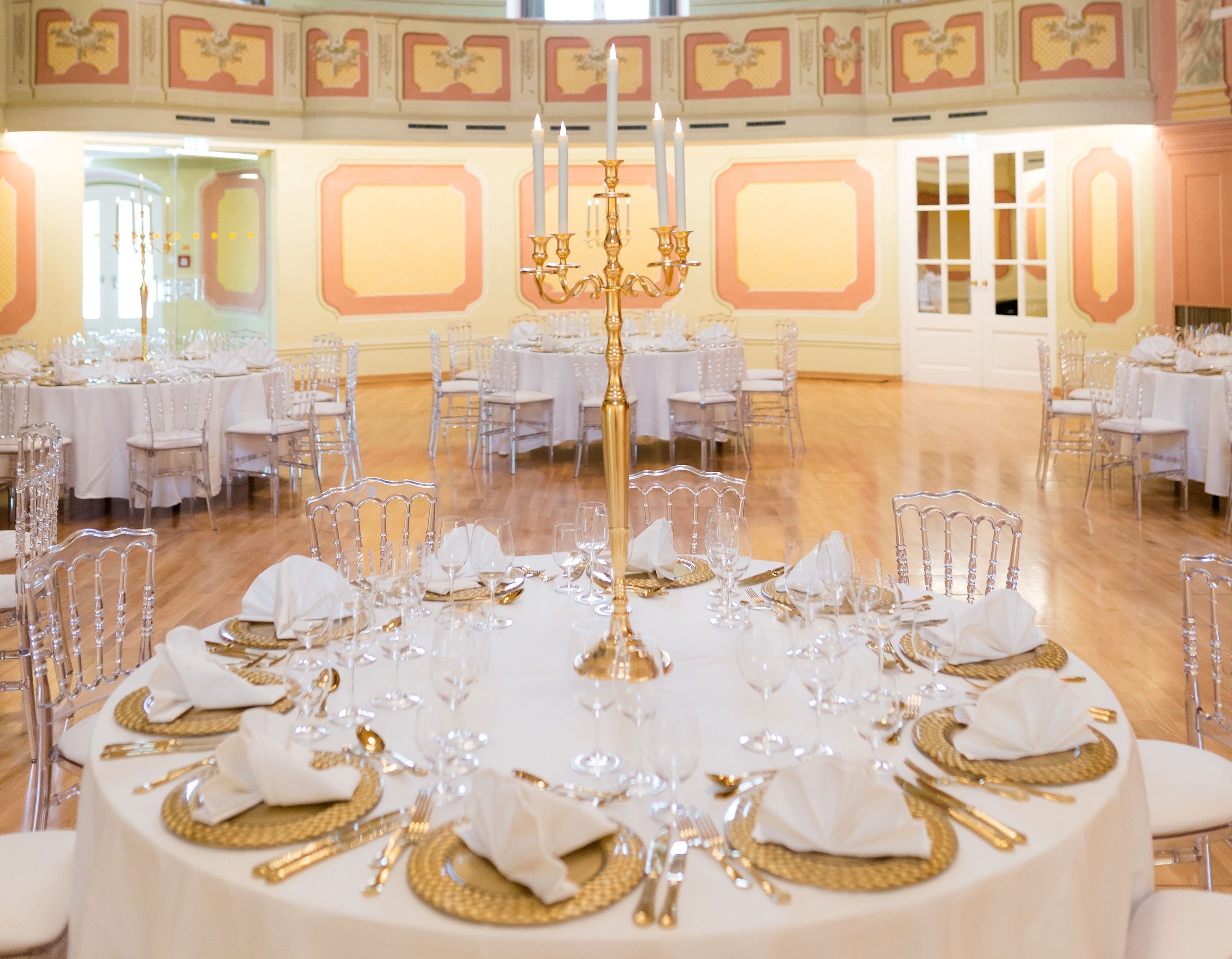 Eleganter Theatersaal mit runden, festlich gedeckten Tischen und goldenen Kerzenhaltern.