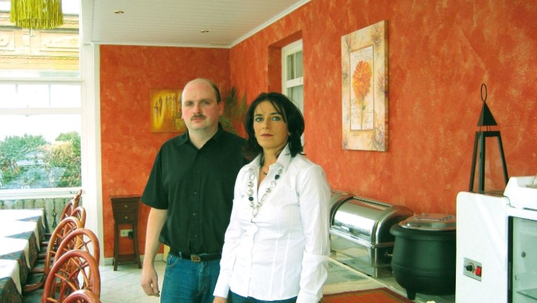 Zwei Personen stehen in einem Restaurant mit orange gestrichenen W&auml;nden.