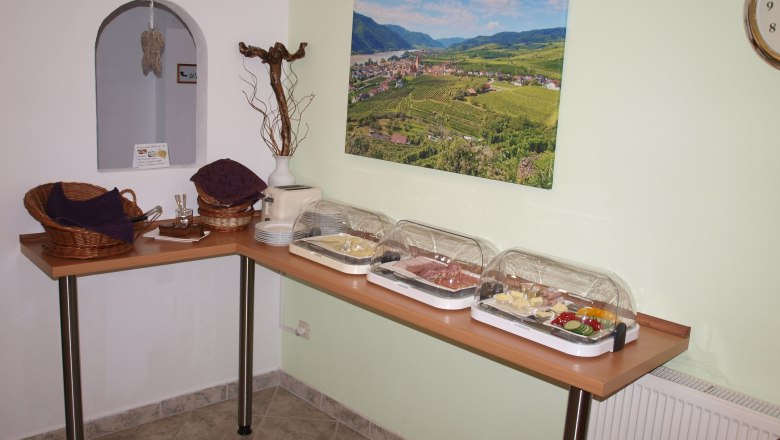 Frühstücksbuffet mit Aufschnitt und Gemüse in einem Raum mit Landschaftsbild an der Wand.