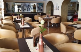 Innenansicht eines stilvollen Cafés mit beigen Sesseln und dekorativen weißen Blumen an der Decke.