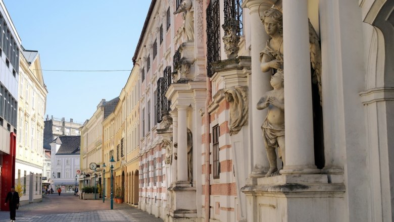 Straße mit historischen Gebäuden und Statuen in einer Stadt.