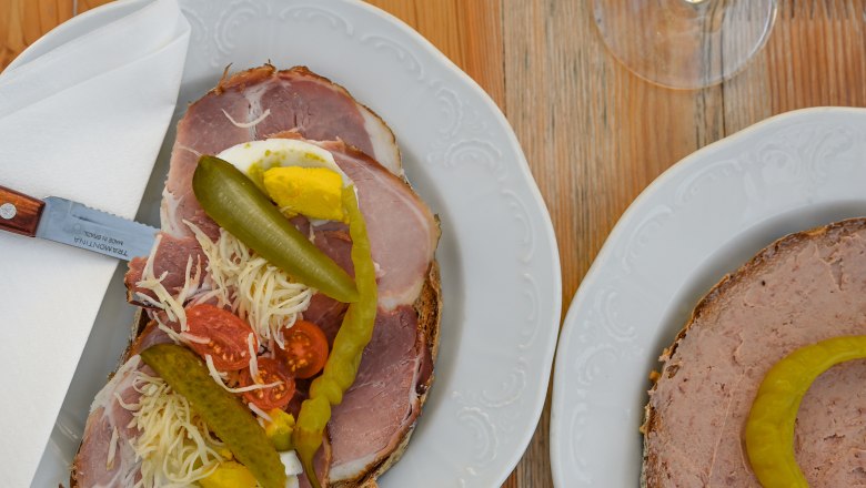 Zwei Teller mit belegten Broten und zwei Gl&auml;ser Wei&szlig;wein auf einem Holztisch.