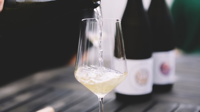 Wei&szlig;wein wird in ein Glas auf einem Tisch eingeschenkt.